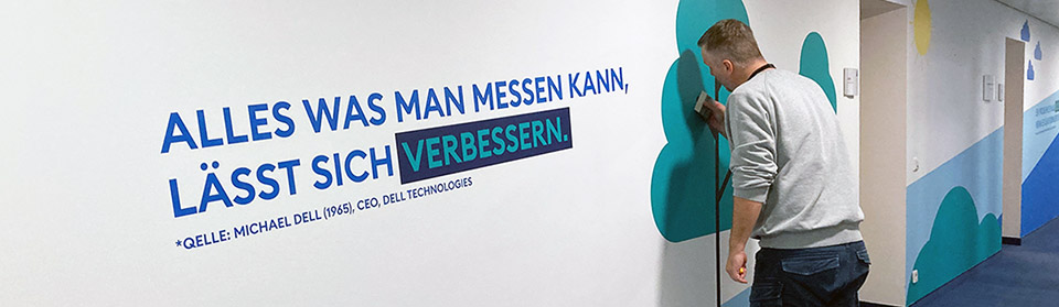 Mitarbeiter bringt Wandgrafik im Büro an – Gestaltung eines Leitsystems für Innenräume